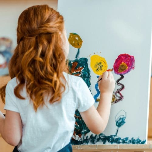 back view of redhead child painting on canvas in art school